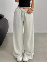 A person wearing light heather gray wide-leg sweatpants with an elastic drawstring waist, paired with a black crop top and white sneakers, standing indoors against a plain light gray wall.