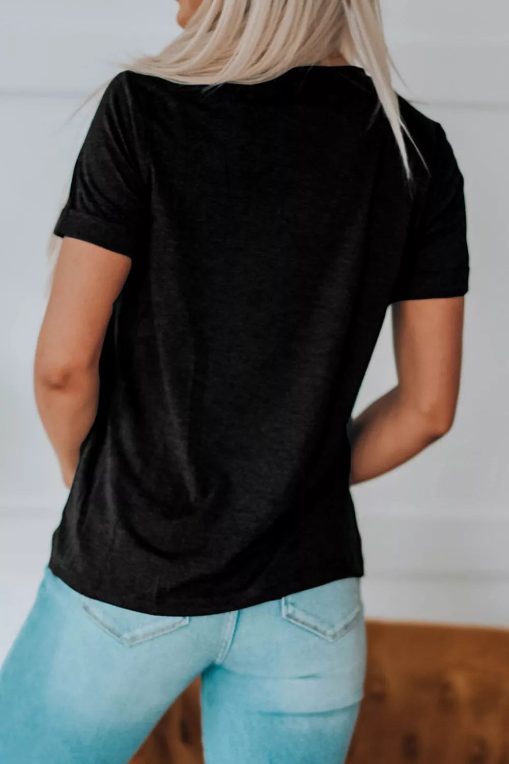 Person wearing a black t-shirt and light blue jeans against a white wall.