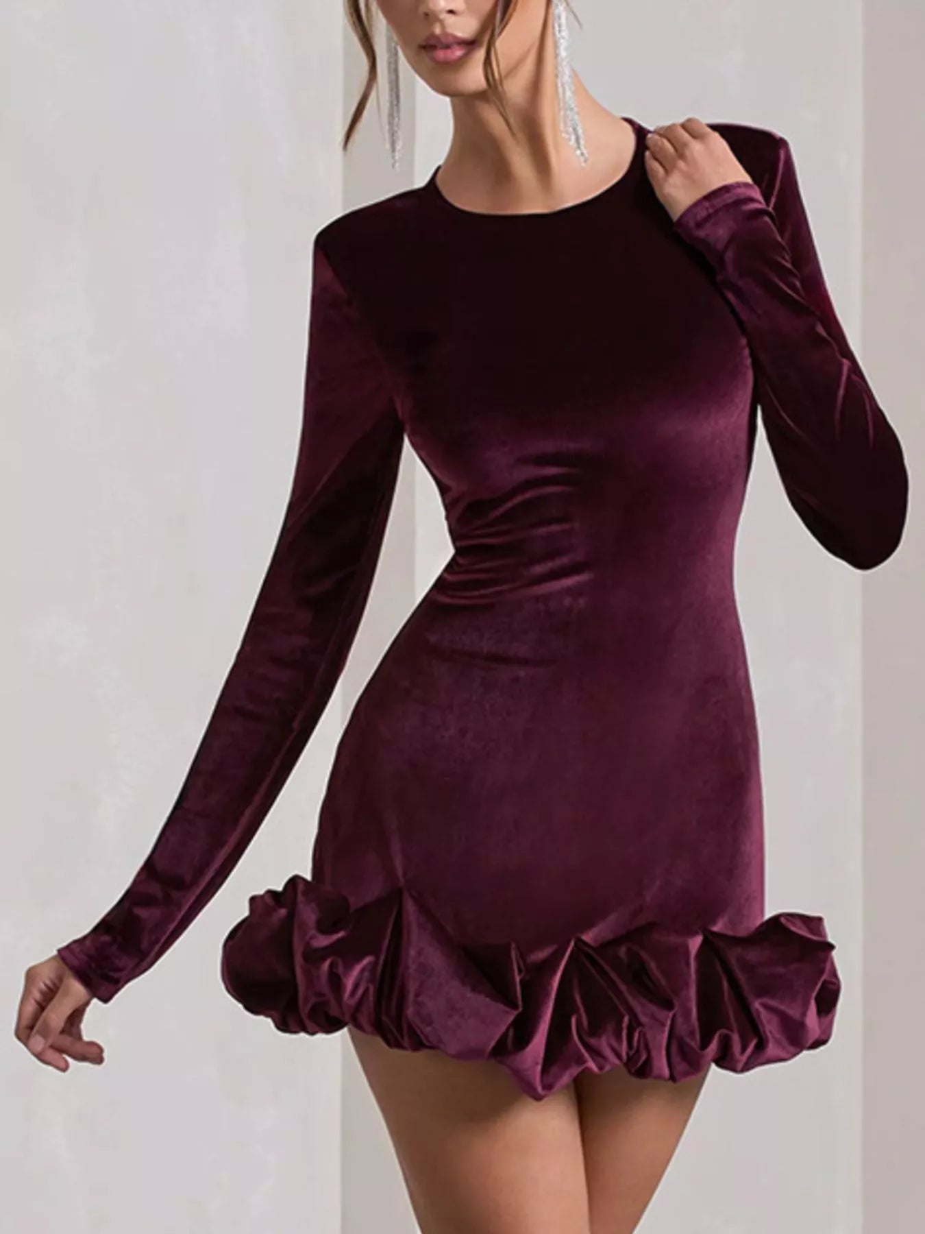 Purple velvet dress with long sleeves and ruffled hem on a plain background