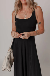 Woman wearing a black dress holding a beige handbag against a neutral background