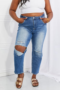 Person wearing ripped blue jeans and a white crop top against a white background
