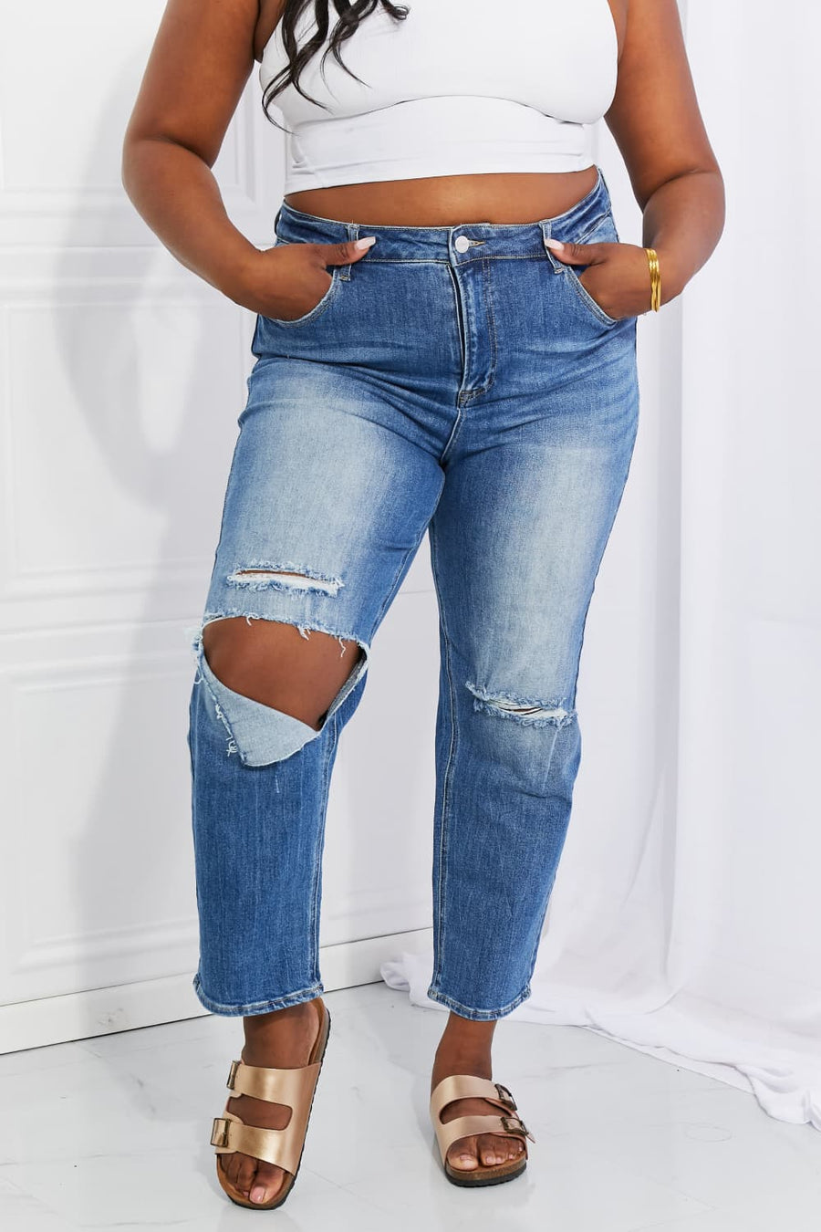 Person wearing ripped blue jeans and a white crop top against a white background