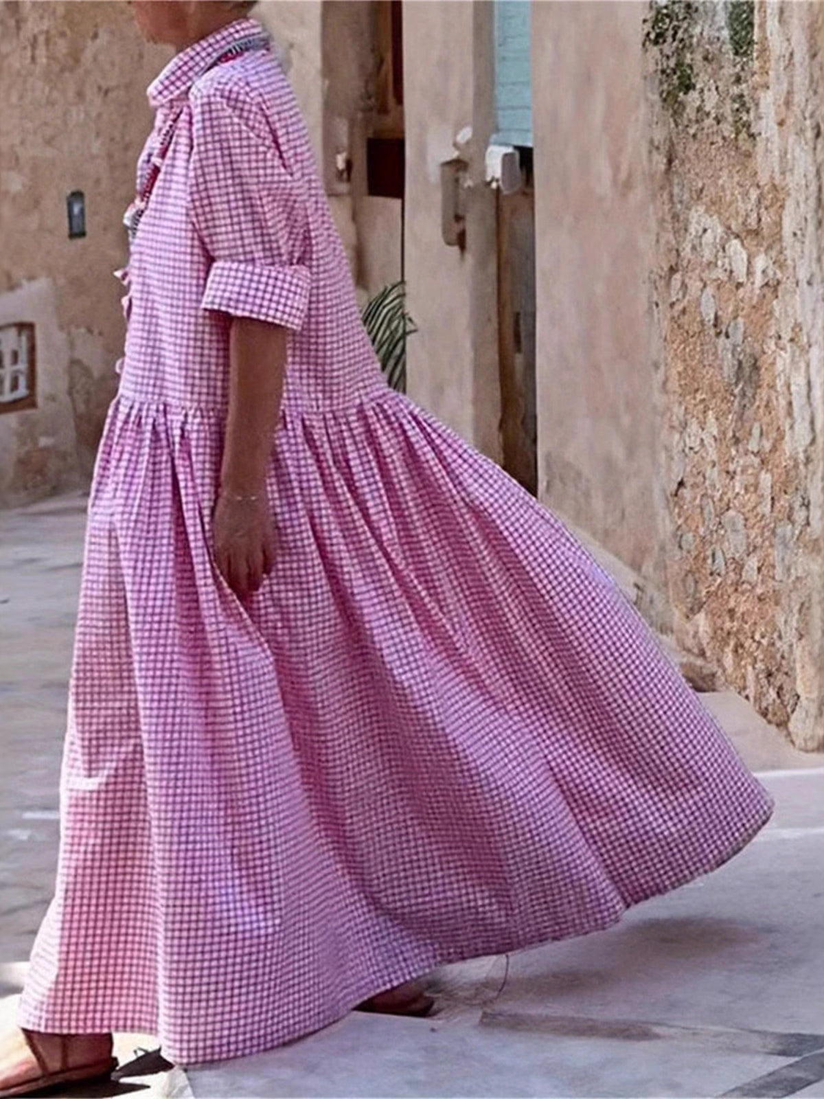 Person wearing a pink checkered dress standing in front of a stone wall.