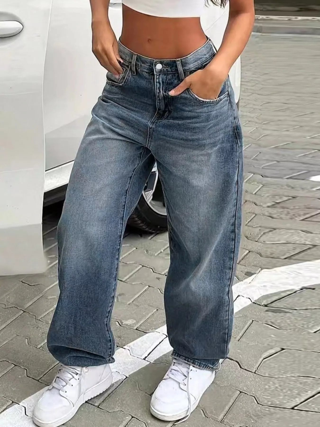 Person wearing blue jeans and white sneakers on a street.