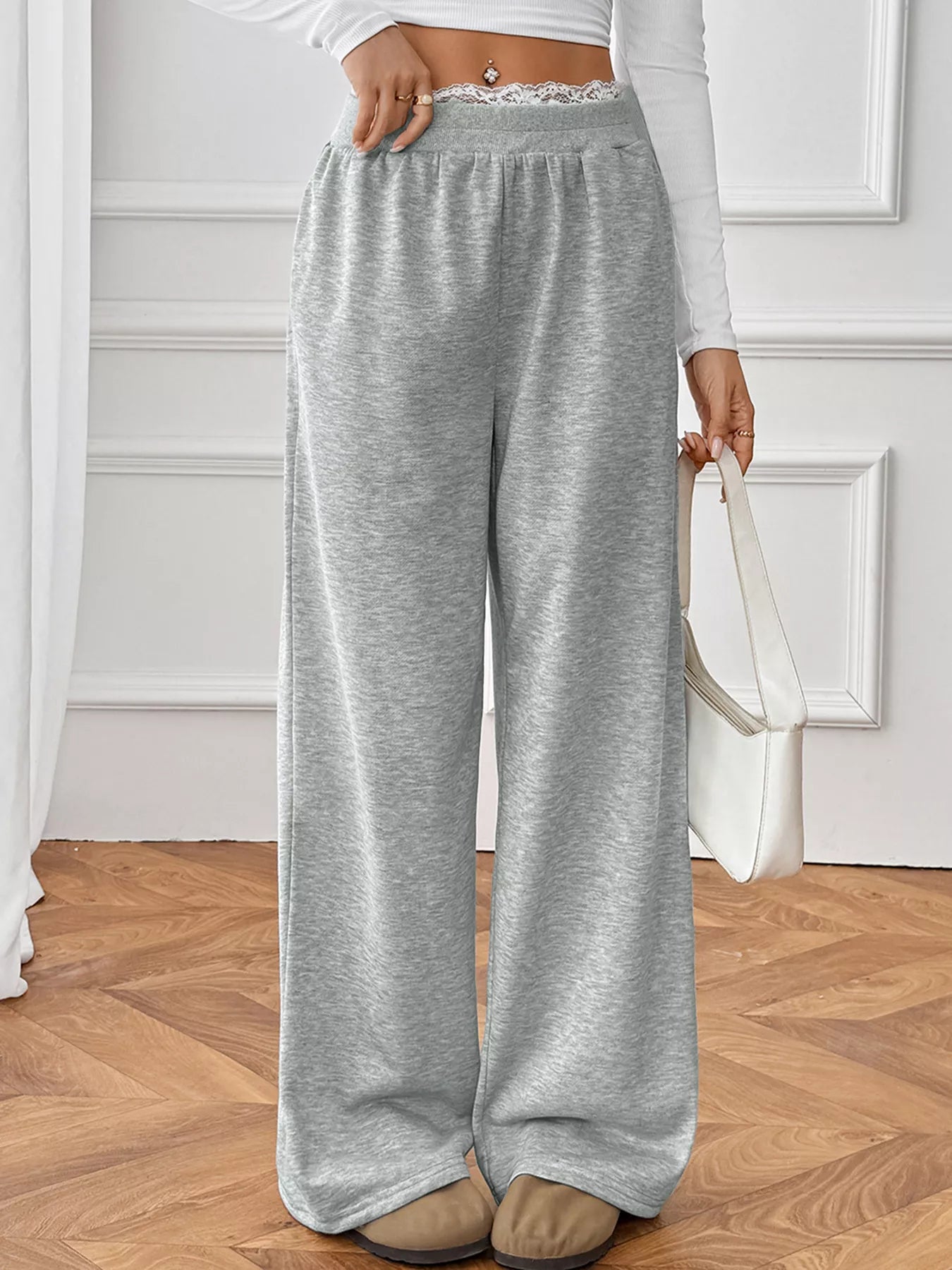 Person wearing gray sweatpants in a room with wooden flooring and white walls.
