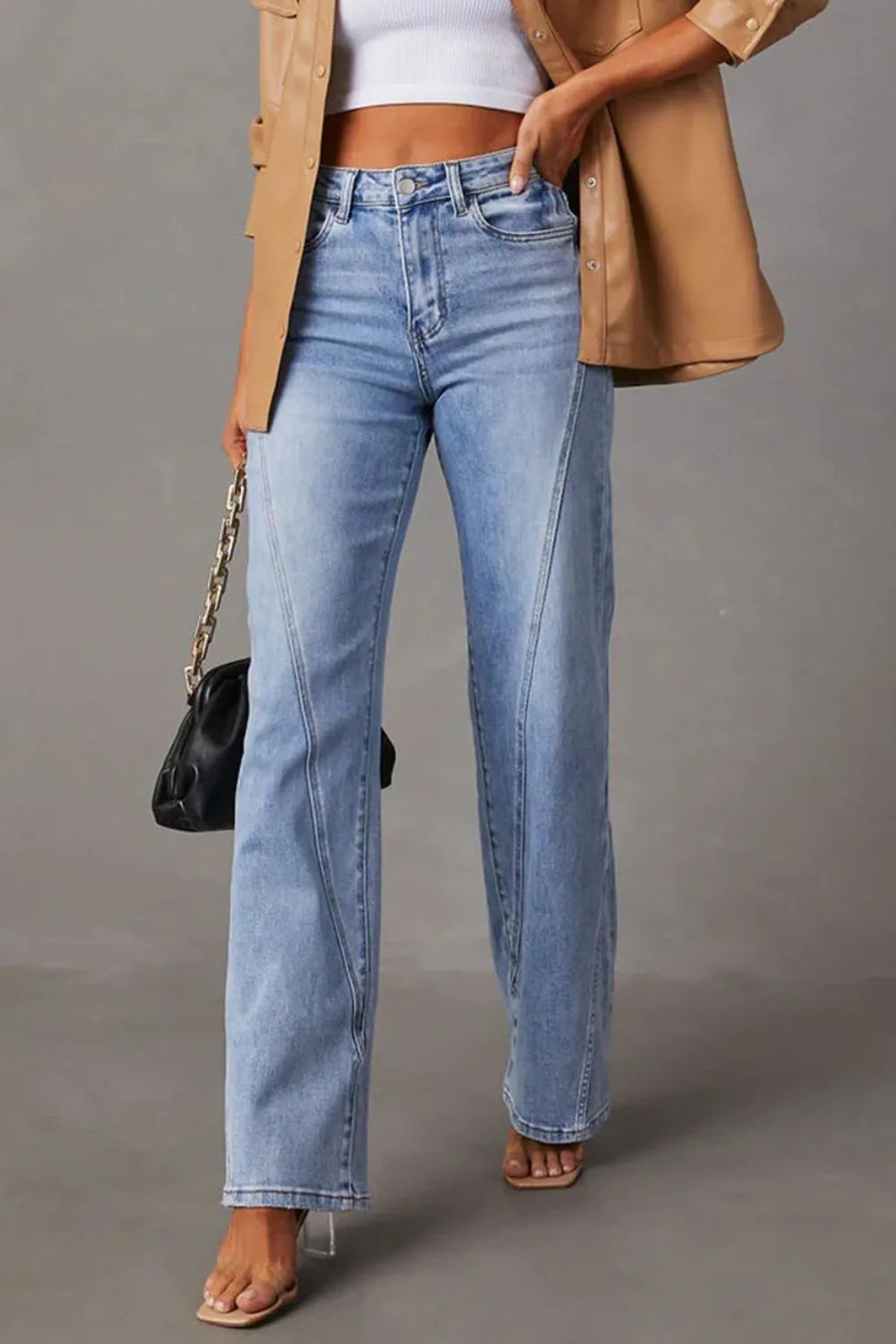 Person wearing light blue jeans with a beige coat and black handbag on a gray background