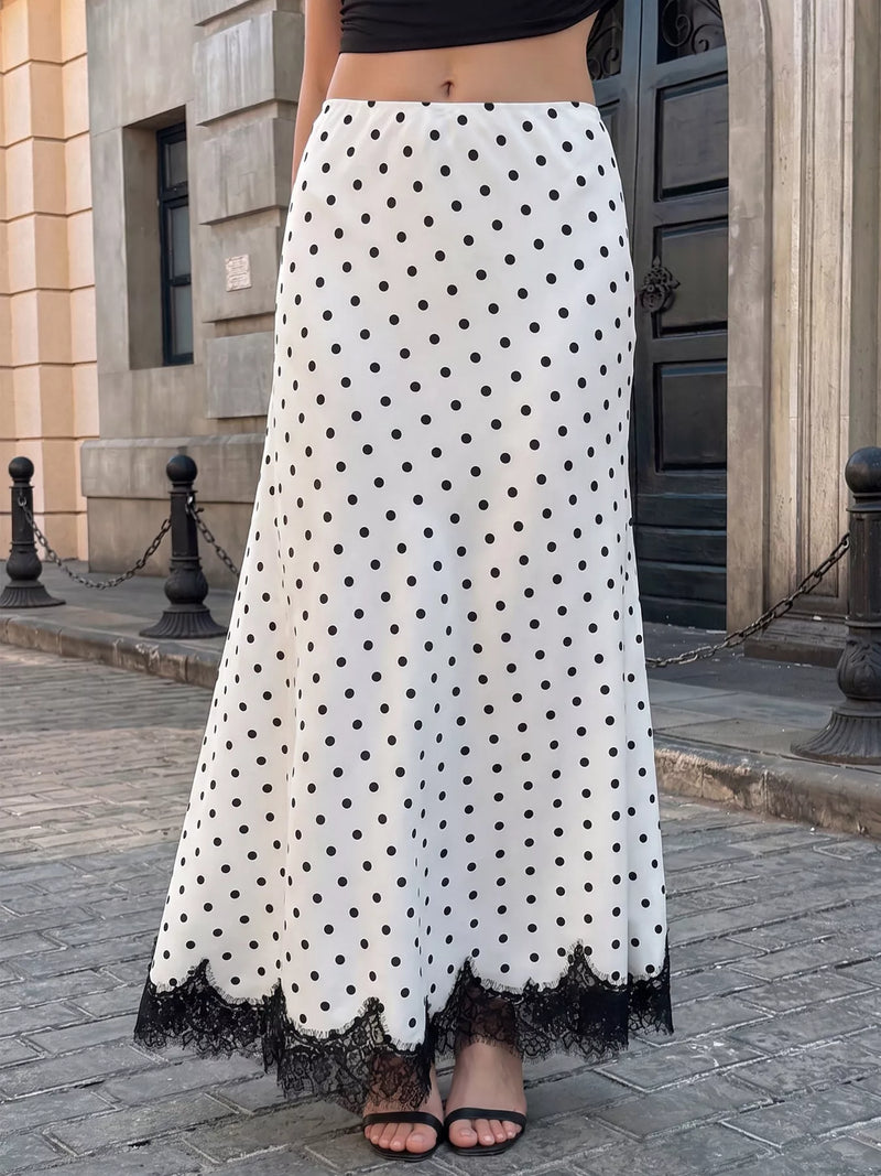 A woman wearing a long white skirt with black polka dots and a black lace hem, paired with black sandals, standing on a cobblestone street in front of a building.