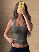 Woman taking a mirror selfie wearing a green tank top against a textured brown wall.