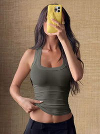 Woman taking a mirror selfie wearing a green tank top against a textured brown wall.
