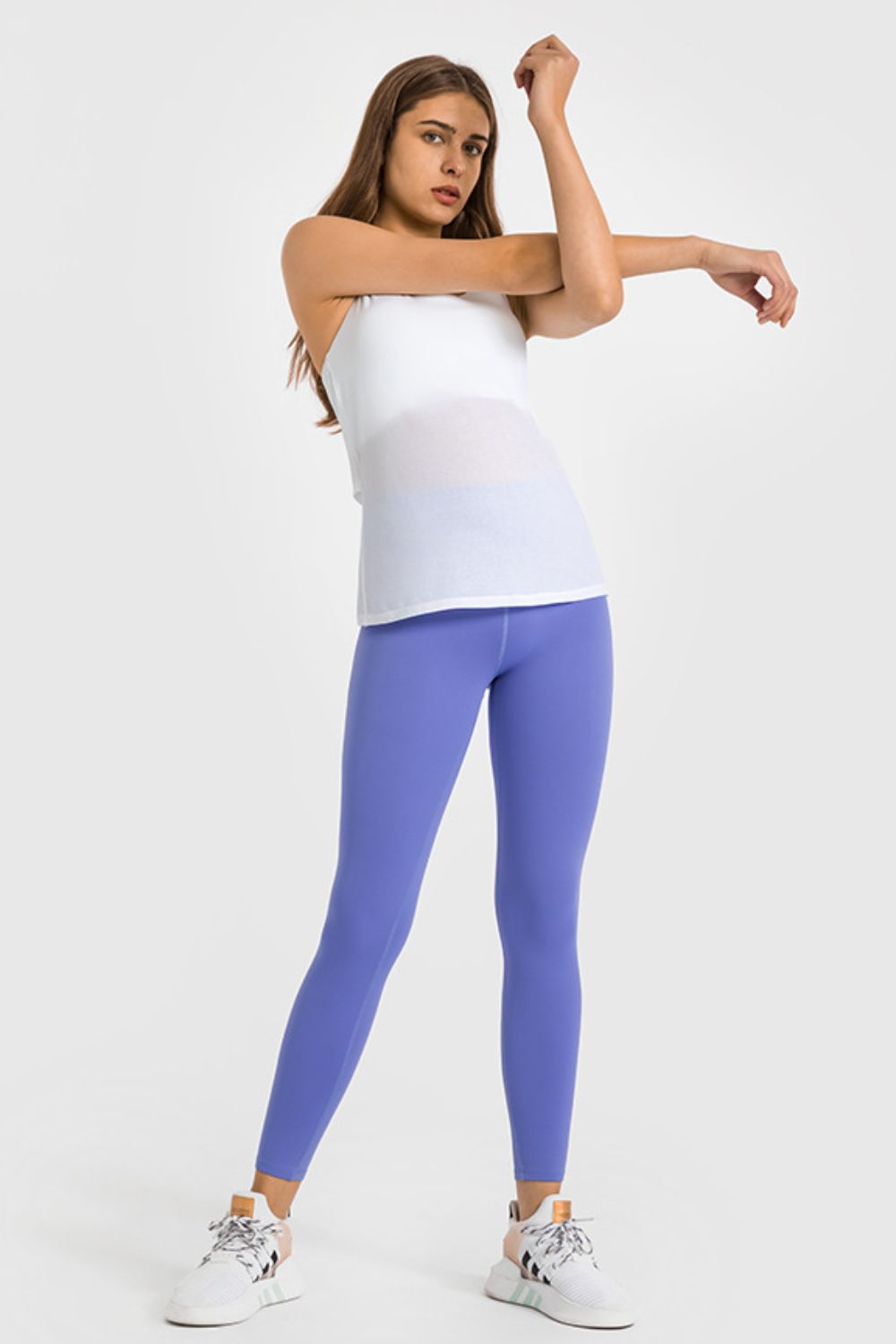 Woman wearing a white tank top and purple leggings on a white background