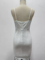 A sleeveless white sequined mini dress with thin shoulder straps, displayed on a beige mannequin torso against a plain light gray wall.