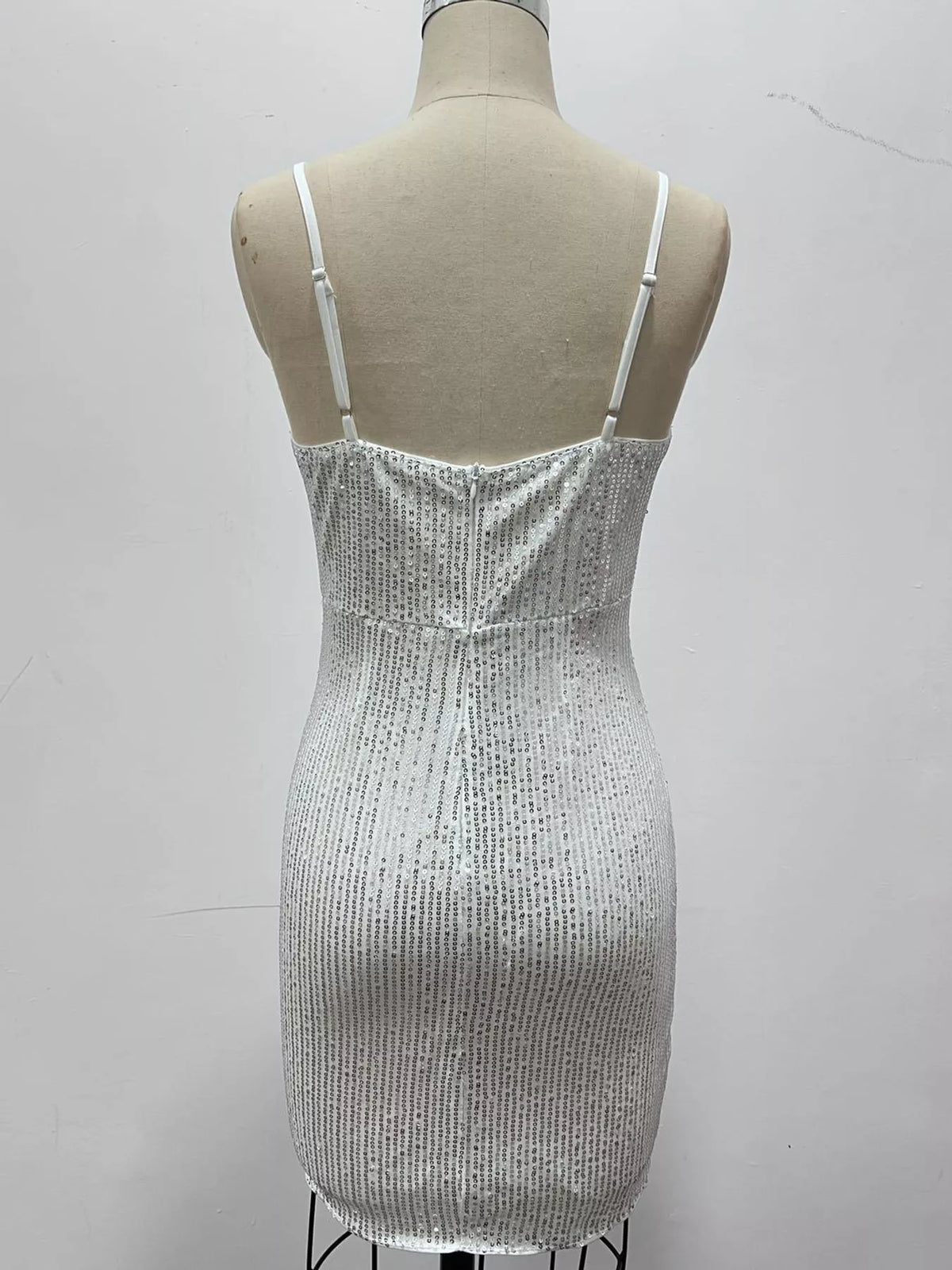 A sleeveless white sequined mini dress with thin shoulder straps, displayed on a beige mannequin torso against a plain light gray wall.