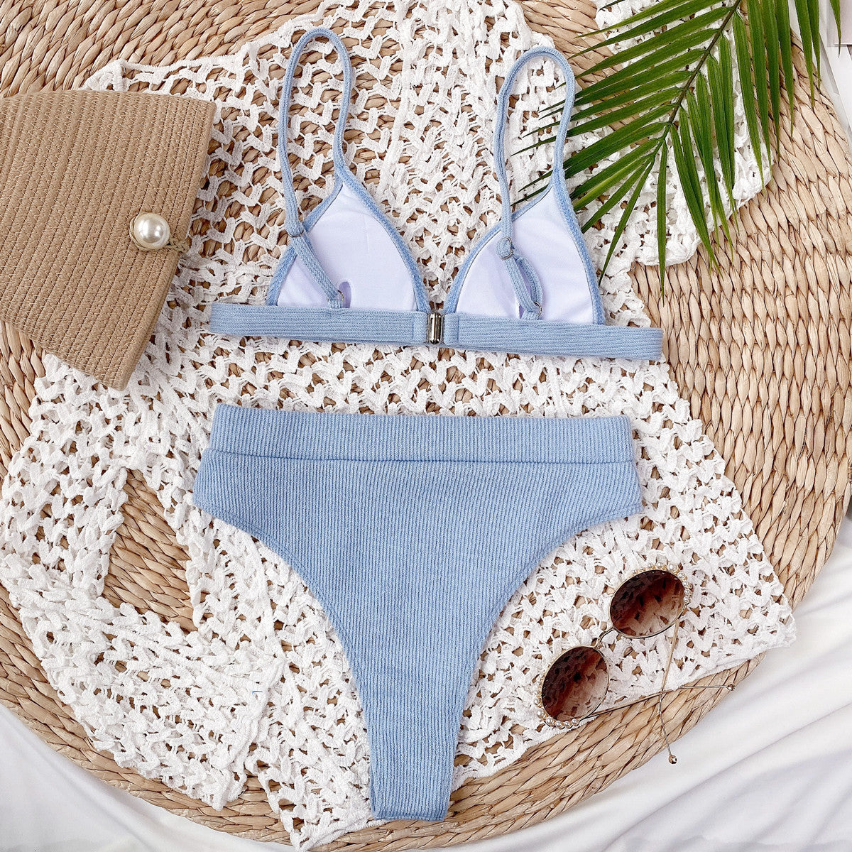 Blue bikini set with a clutch and sunglasses on a textured surface
