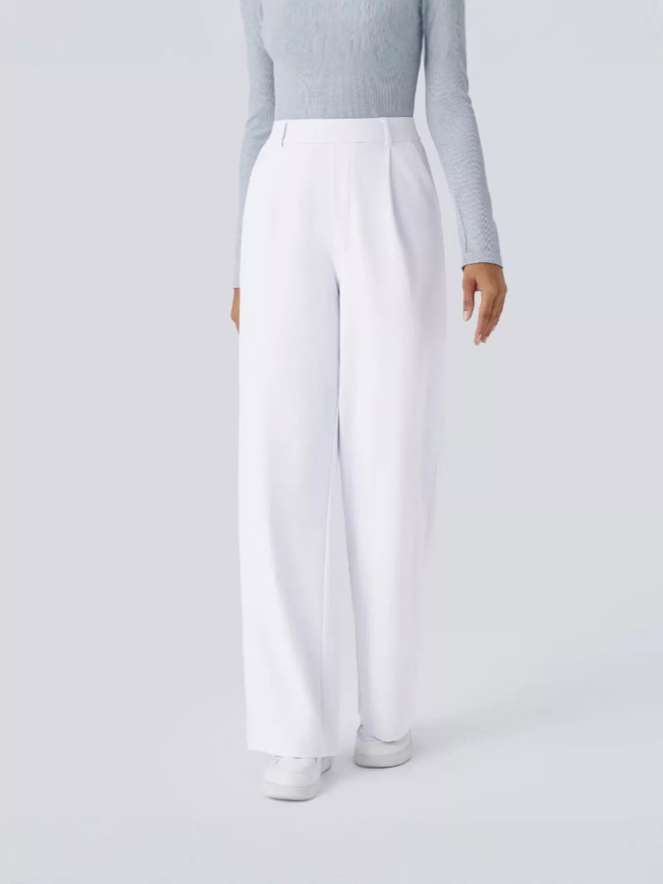 Person wearing light gray long-sleeve top and white pants on a plain background