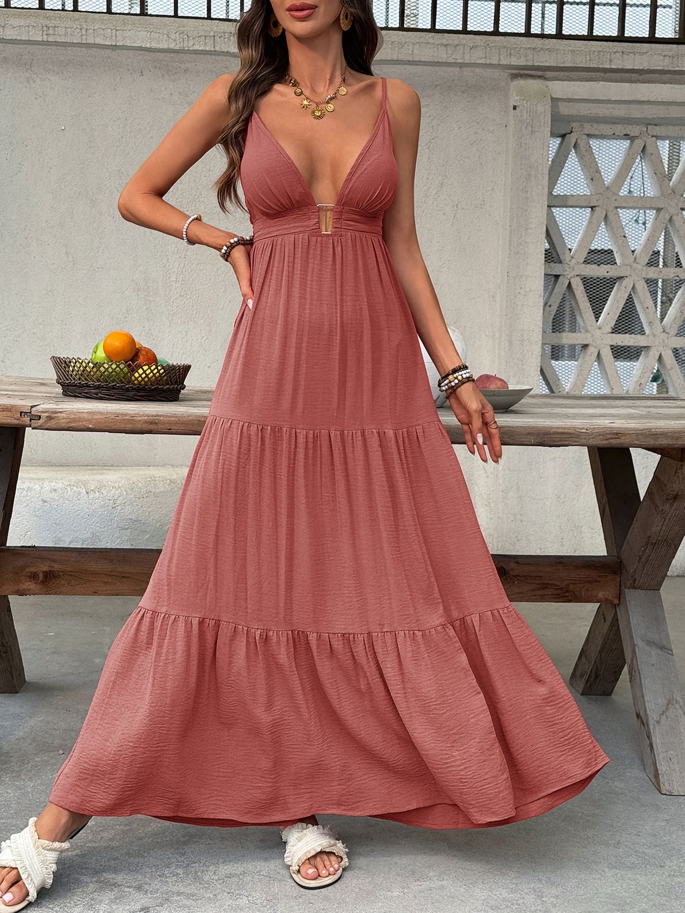 Woman wearing a long pink dress standing in front of a wooden table with fruits.