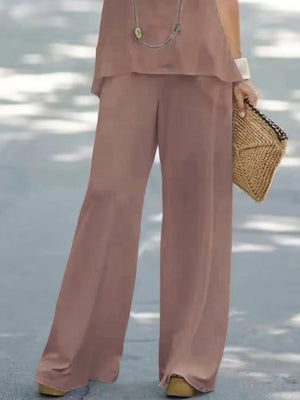 Person wearing a brown outfit with wide-leg pants holding a woven bag on a light background