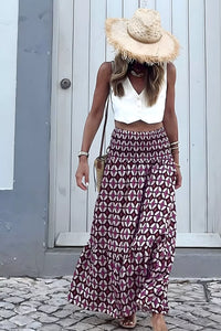 Woman wearing a white top and patterned skirt with a straw hat, standing on a cobblestone street.