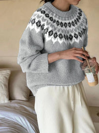 Person wearing a gray sweater with floral patterns, holding a drink, sitting on a couch.