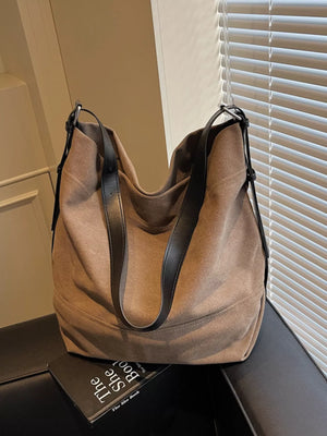 Brown leather handbag on a surface with a book underneath, against a neutral background.