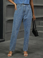 Person wearing blue jeans with pearl embellishments in an urban setting.
