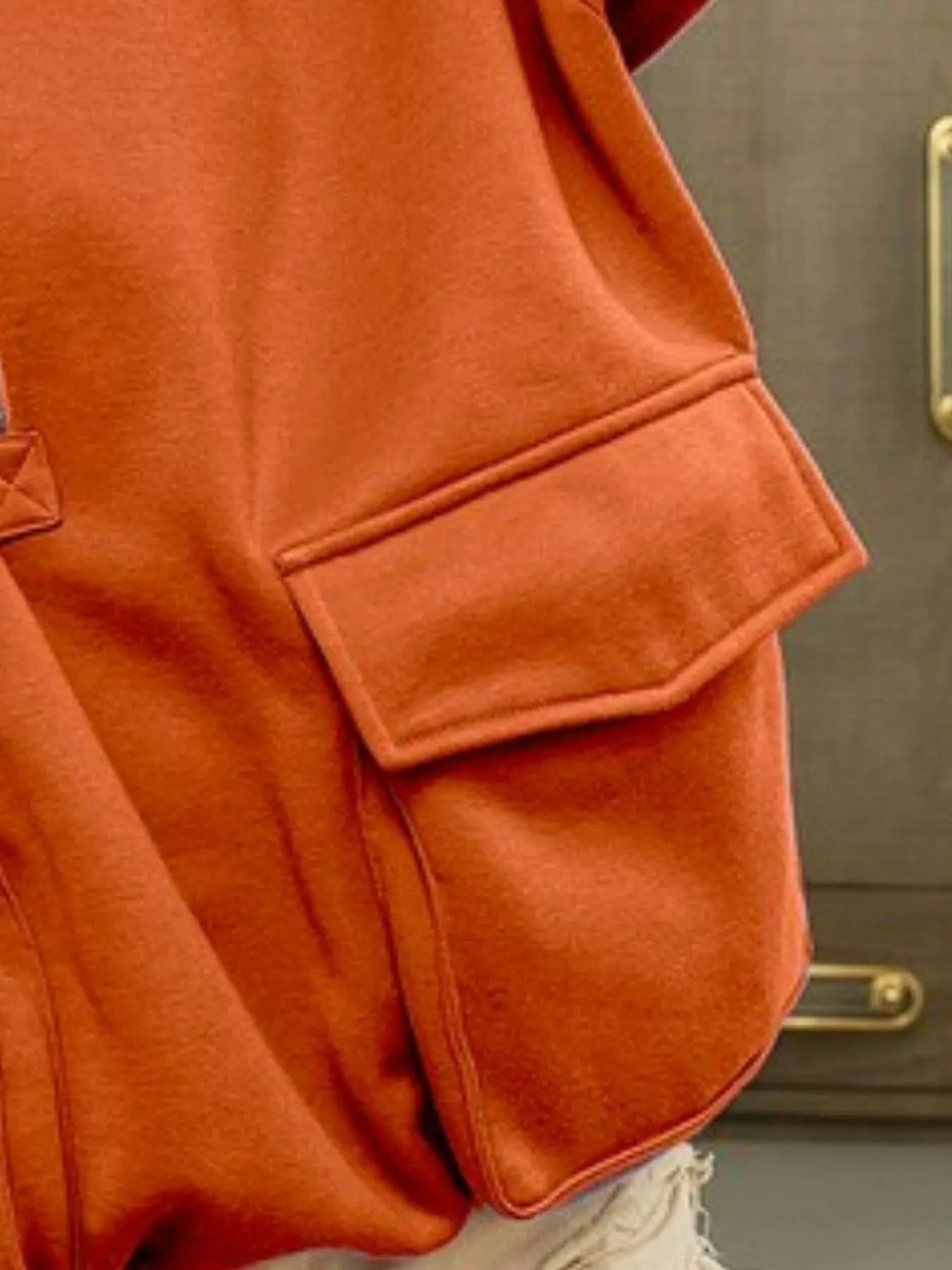 Close-up of an orange jacket with a pocket against a neutral background