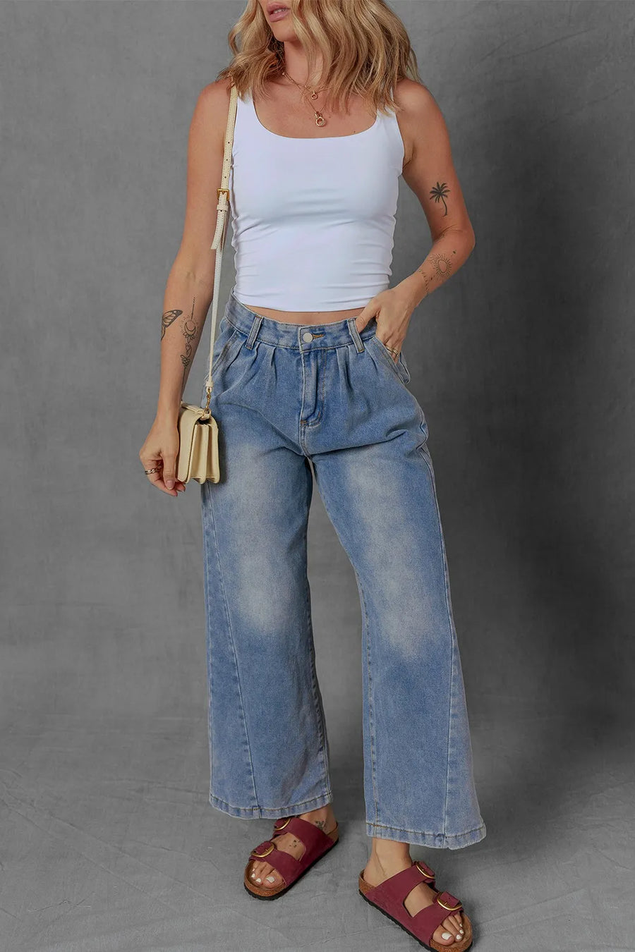 Woman wearing a white tank top and blue jeans against a gray background