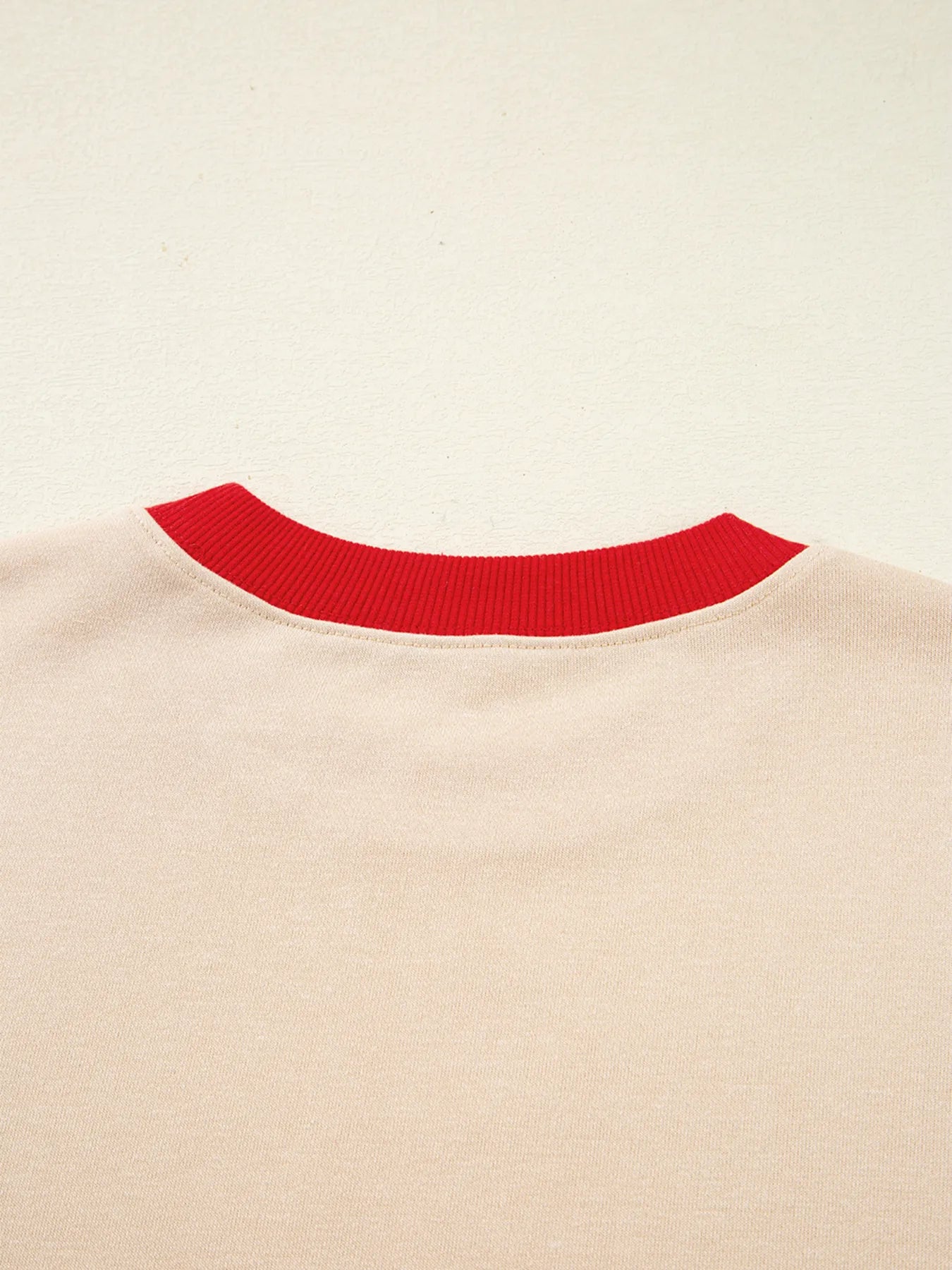 Close-up of a beige sweater with a red neckline on a beige background