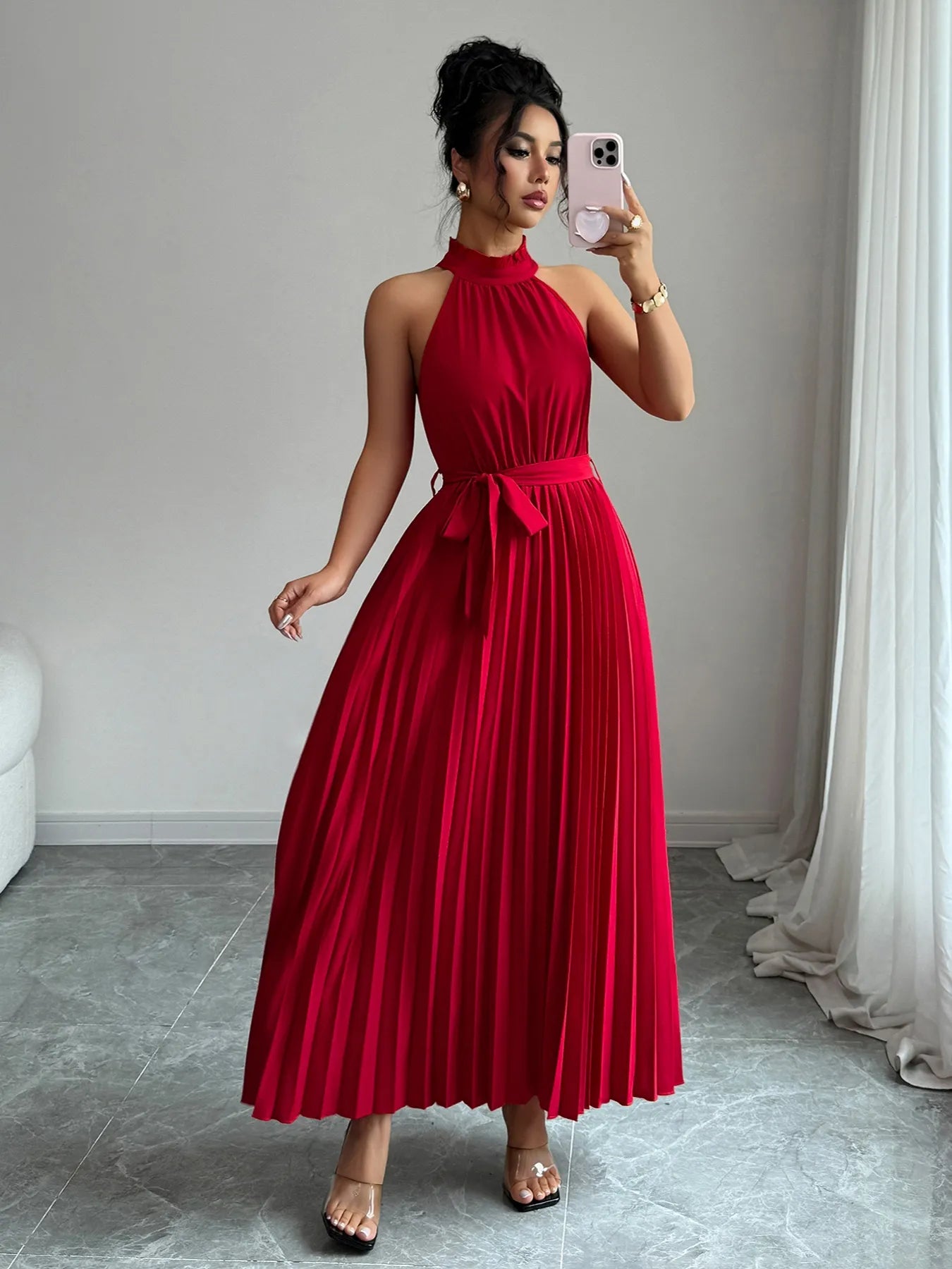 Woman wearing a red dress taking a mirror selfie in a room with a gray floor and white walls.