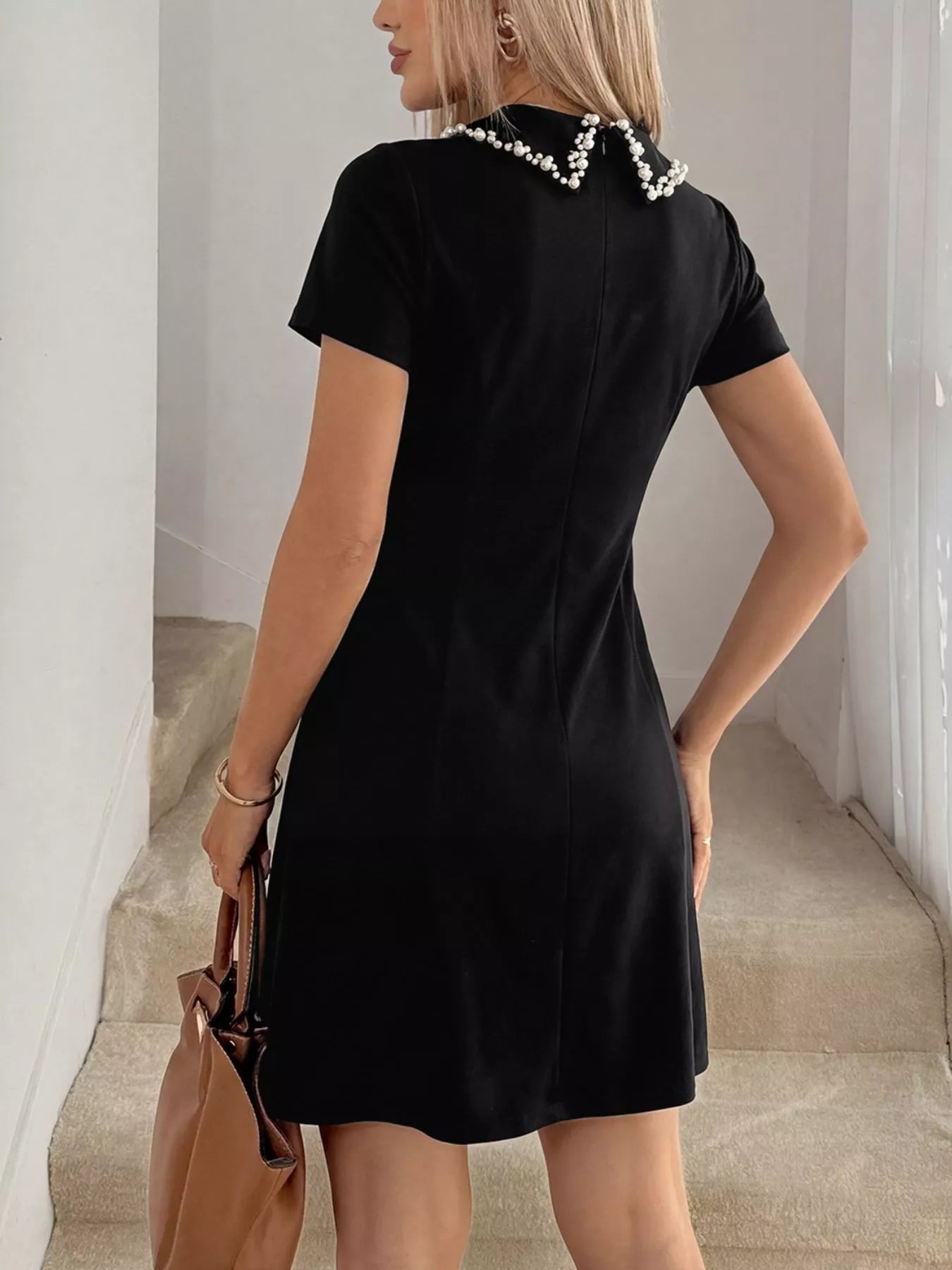 Woman wearing a black dress with pearl details in an indoor setting