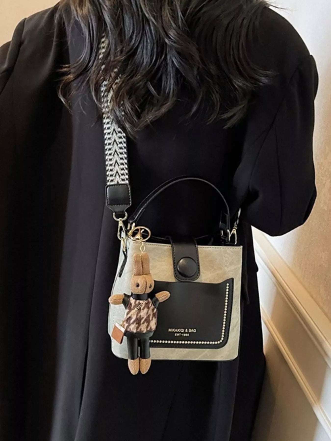 Person wearing a black outfit with a small handbag featuring a teddy bear keychain.