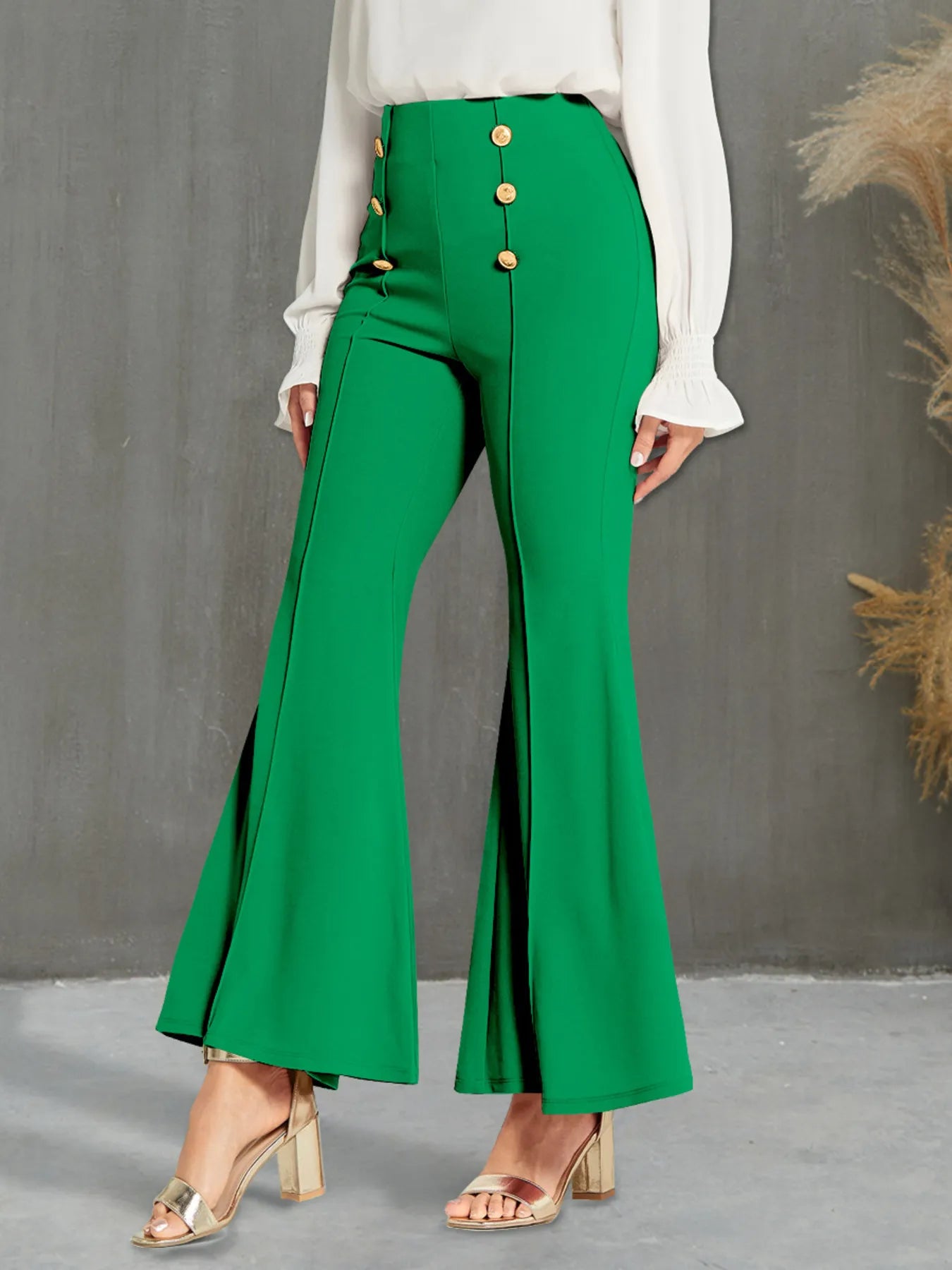 Green flared pants with gold buttons worn by a person against a gray background