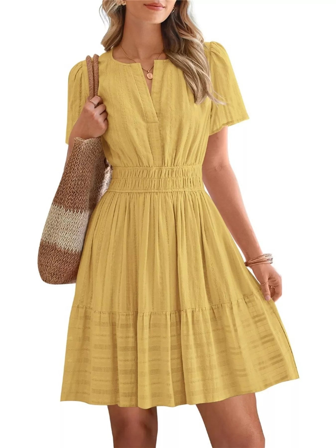 Woman wearing a yellow dress holding a brown and beige striped bag on a white background