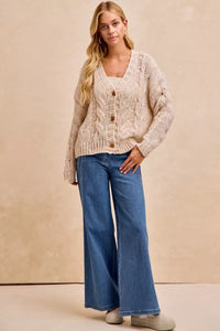 Woman wearing a beige cardigan and blue jeans against a beige background