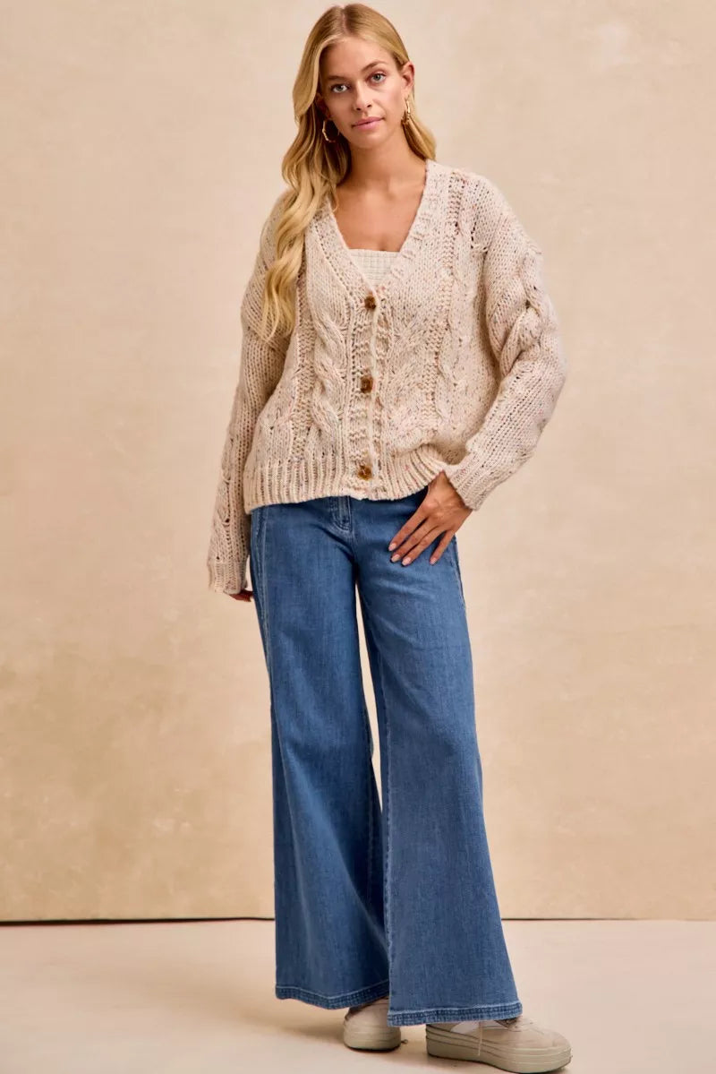 Woman wearing a beige cardigan and blue jeans against a beige background