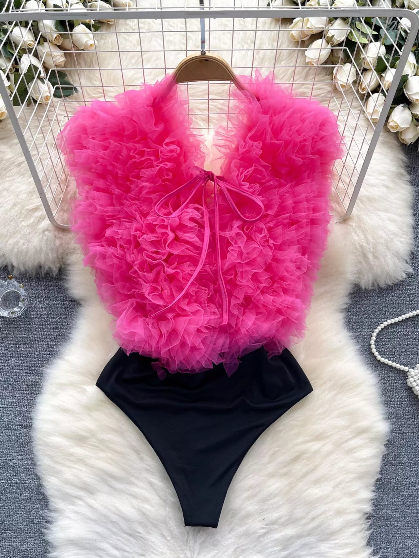 Pink ruffled top and black high-waisted bottom set on a white fur surface with decorative background.