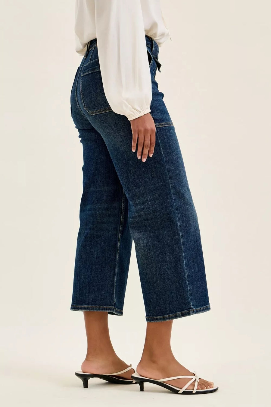 Person wearing blue jeans and a white top on a plain background