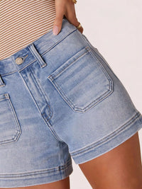 Close-up of a person wearing light blue denim shorts on a plain background