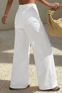 Person wearing white wide-leg pants holding a straw bag on a textured surface.