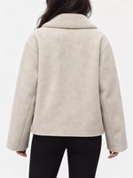 A person shown from the back wearing a light beige sherpa or fleece jacket with a wide collar and long sleeves, paired with black pants, against a plain white studio background.