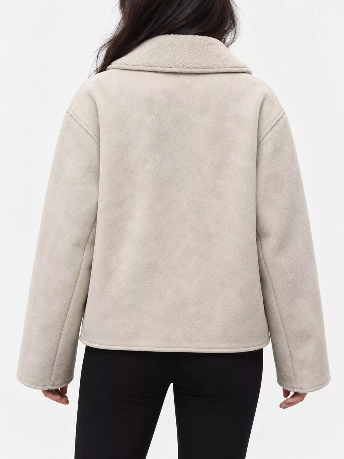A person shown from the back wearing a light beige sherpa or fleece jacket with a wide collar and long sleeves, paired with black pants, against a plain white studio background.