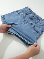 Person folding a pair of blue denim shorts on a white surface