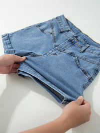 Person folding a pair of blue denim shorts on a white surface