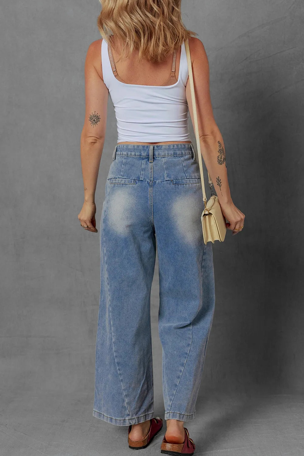 Person wearing a white tank top and blue jeans against a gray background