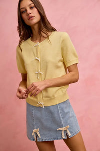 Woman wearing a yellow cardigan and denim skirt with a pink background