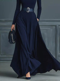 Person wearing a long navy dress with a belt against a gray paneled wall.