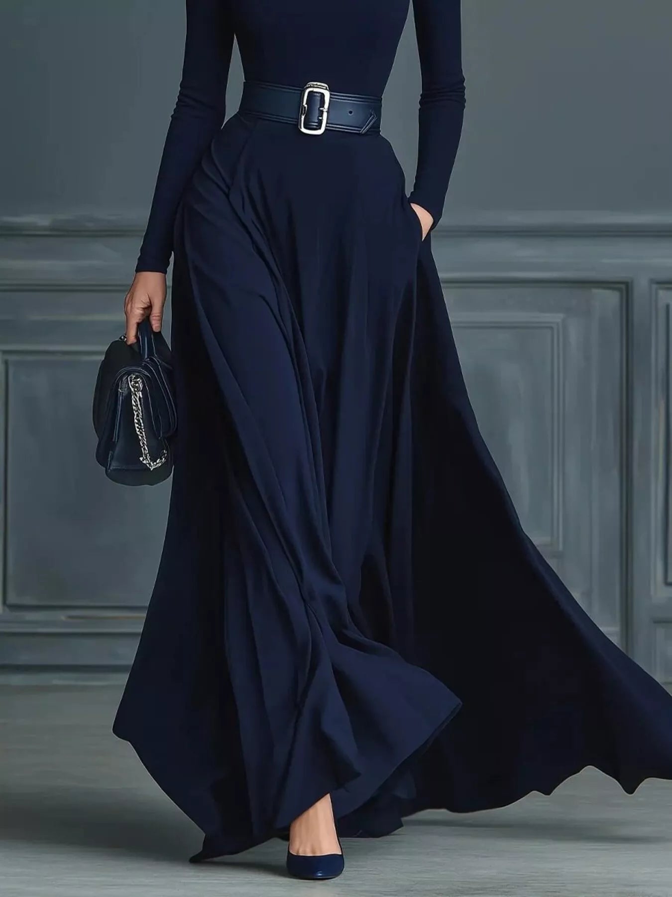 Person wearing a long navy dress with a belt against a gray paneled wall.