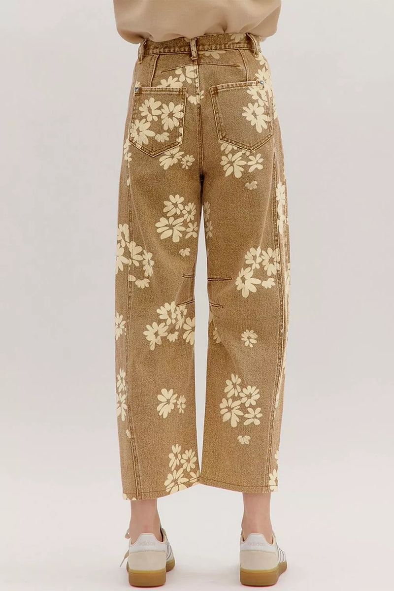 A person shown from the waist down wearing tan wide-leg cropped jeans with a cream floral pattern, paired with white sneakers, against a light gray studio background.