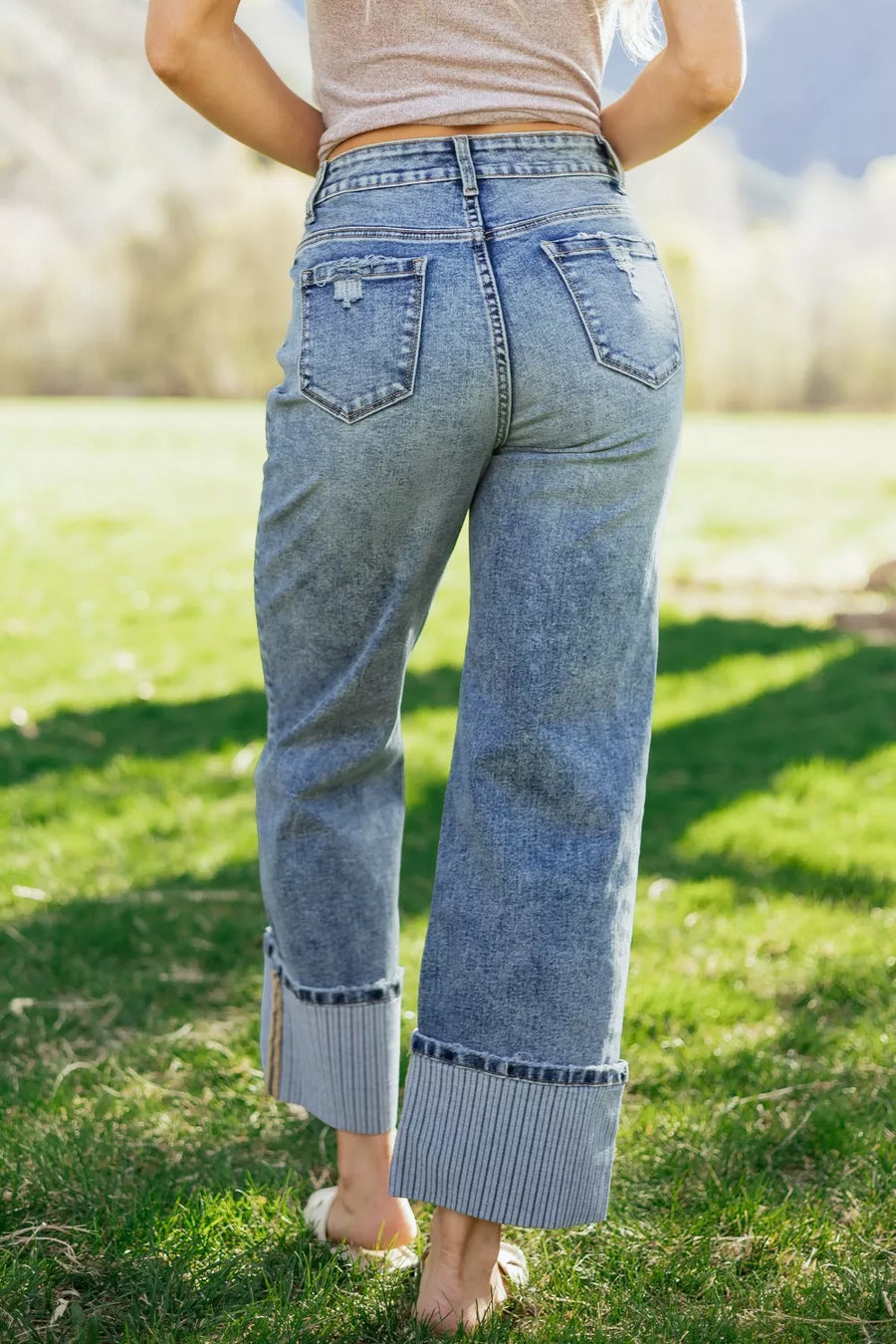 Person wearing high-waisted blue jeans standing on grass with a blurred background