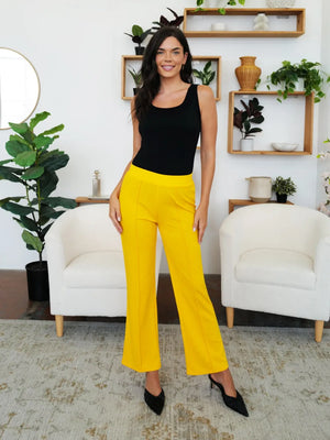 Woman in black top and yellow pants standing in a modern living room.