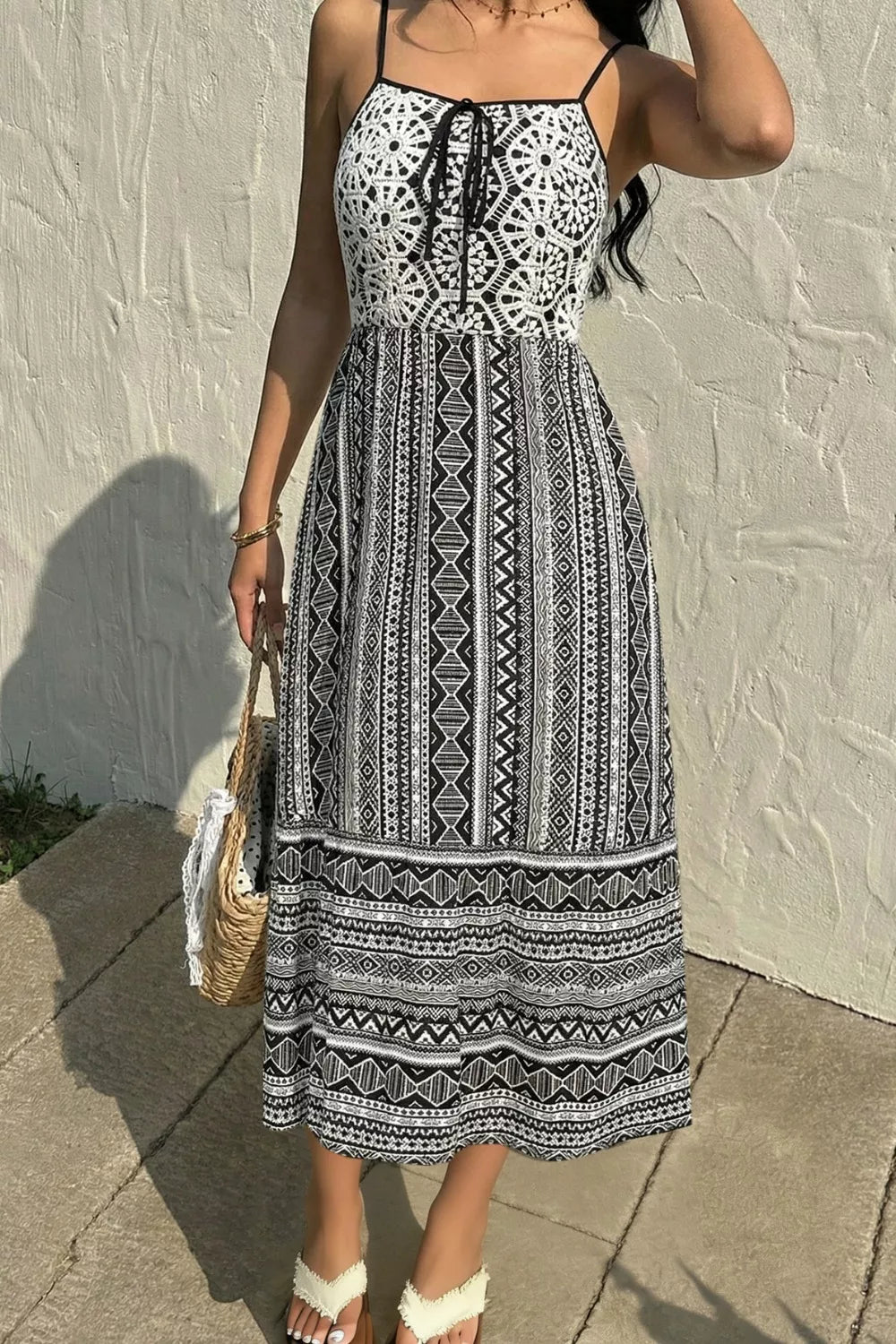 Woman wearing a black and white patterned dress against a light-colored wall.